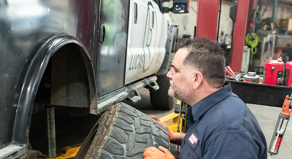 Diesel Pros technician inspecting the rear wheel and suspension of a lifted truck