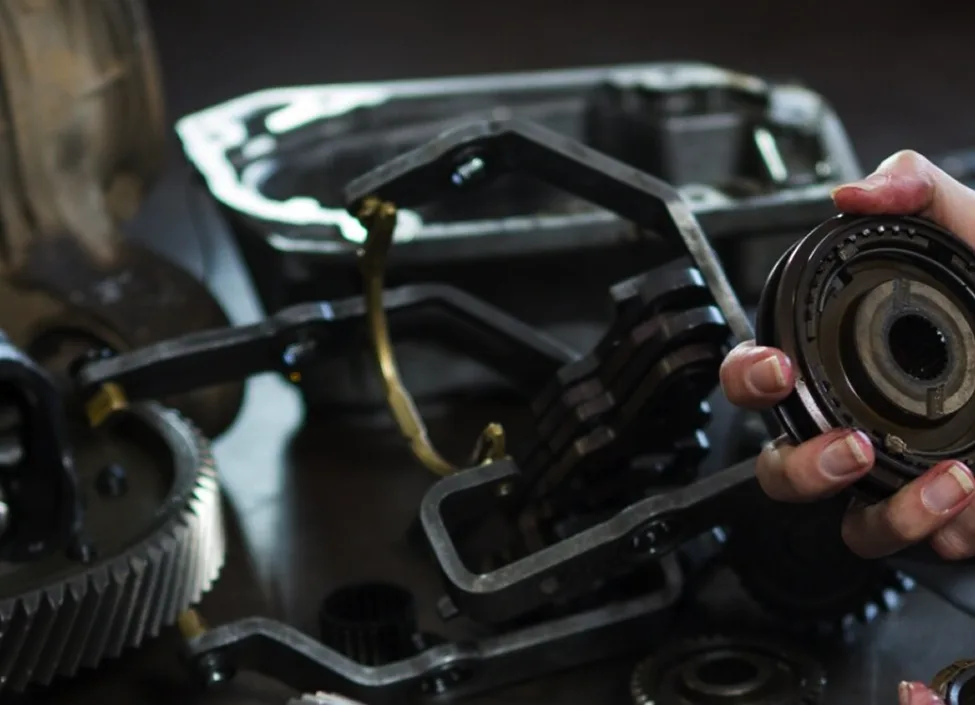 Technician holding a transmission component over a disassembled diesel gearbox during a rebuild